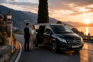 Mercedes V-Class with professional chauffeur assisting passengers during a luxury long-distance transfer on a scenic lakeside road in Italy.