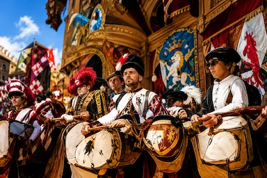Traditional drummers in historical costumes during the Palio di Siena parade, with colourful contrade flags.